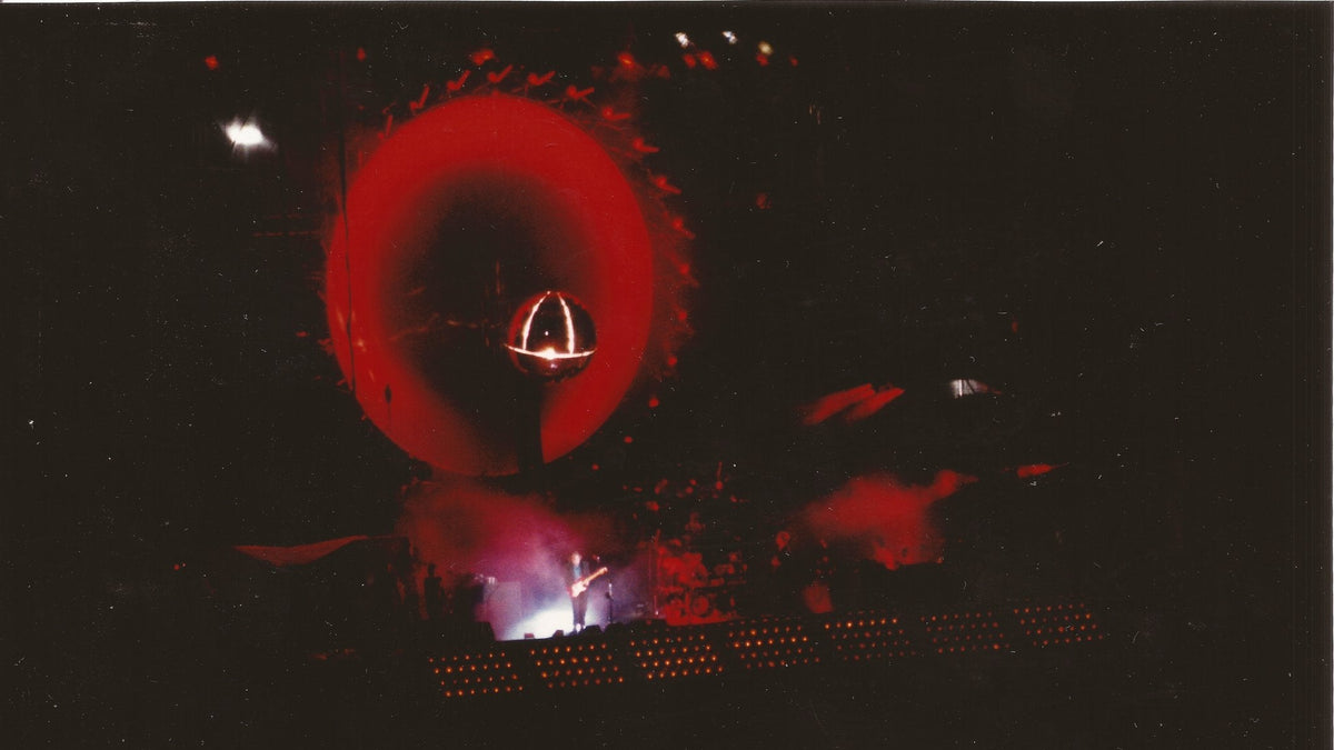 Pink Floyd live on stage in Toronto with the band's iconic circular screen glowing red behind the guitarist