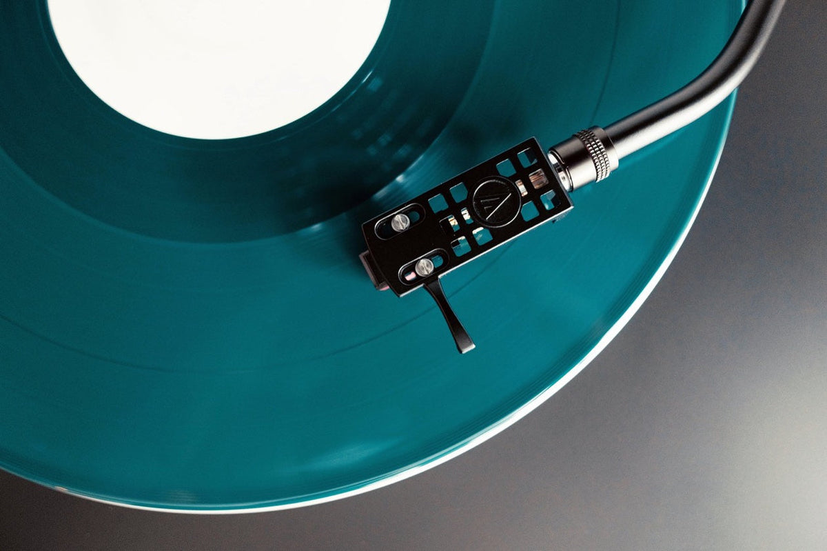 Teal coloured vinyl record on a turntable with the tonearm and cartridge resting on the disc